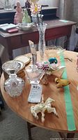 View of perfume bottles, Radnor porcelain flowers, crystal bud vase, depression glass bowl, and porcelain animal figurines arranged on wooden table.