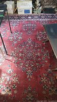 Full view of rug showing central red field with floral medallions amid surrounding furniture and storage boxes