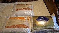 Three white down pillows on bed, two in Strasbourg packaging, one in Hampton Feather packaging