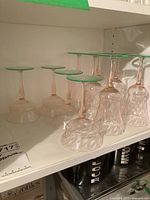 Five inverted and upright pink-and-green stemware glasses on a white shelf showing overall grouping and colors.