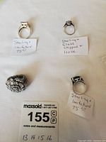 Four rings displayed on white background including three sterling silver rings with imitation stones and one large sterling silver flower-shaped ring with clear stones.