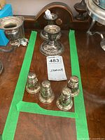 Top photo of two sets of sterling salt and pepper shakers with two candle holders on a wooden surface.