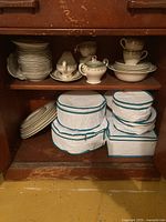 Shelf with stacked plates, teacups, saucers, sugar bowl and gravy boat, plus cloth covers below
