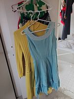 Blue sleeveless gingham dress with white trim and a yellow knit dress/sweater on hangers