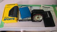 Lot laid together showing all items: Sony Walkman Sports cassette player, blue Holiday micro radio, Westclox travel clock, and Panasonic microcassette recorder with manual.