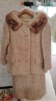 Full view of vintage bouclé dress and matching double-breasted jacket with faux fur collar hanging on hanger.