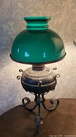 Full view of vintage table lamp showing green glass shade and metal base with scrollwork.
