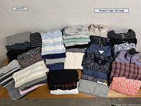 Photo showing folded assortment of women's large tops with various patterns and colors on table.