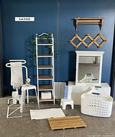 Full view of all bathroom organizing items including shelves, stools, towel hanger, basket, hooks, rugs, and mats against a blue wall.