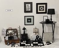 Display of the lot showing small black folding table holding a black lamp, three monochrome floral artworks, and various black and white decorative items arranged below and around the table including a striped pillow, black bead placemats, trays, and small decor pieces