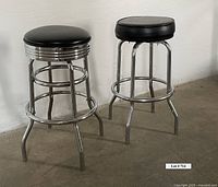 Two black and chrome workshop stools from a side angle with one showing ribbed chrome detail under the seat.