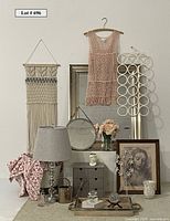 Full lot view showing macrame wall hanging, pink crocheted top, vase with faux roses, framed artwork, glass ball lamp, mirrors, storage cubbies, and various decor items arranged on and around a small storage drawer unit with a lamp.