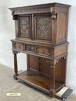 Front-angle view of carved oak chiffonaire showing floral carved doors, drawers, turned columns and bottom shelf.
