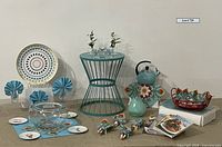 Full view of the teal metal side table with party items arranged around it including napkins, glasses, plates, vase, teapot, basket, tray, cookbooks, and glass bowl.