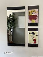 Photo showing two Cordell Cordaro prints mounted vertically on a wall next to a tall contemporary mirror with black trim top and bottom. The prints feature imaginative female portraits in vibrant colors.