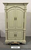 Front view of the large painted pine Country French armoire showing upper and lower doors with brass handles and crown molding.