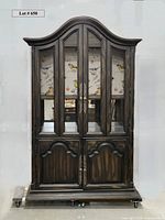 Front view of the dark wood armoire showing arched top, mesh wire doors with bird motif interior, and solid lower doors.