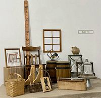 Photo showing various farm style decor items atop table with wooden chair, barrel stools, picnic basket, cloche, iron horse head knocker, rooster figure, trug, glass jug lantern, wooden ruler, framed quilt print, wooden trug, wooden shelf brackets.