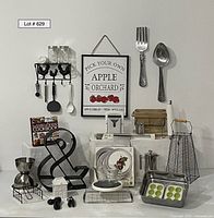 Full view of farmhouse kitchen items including wall sign, wire basket, large fork and spoon, wall hooks, cookware, and kitchen gadgets.
