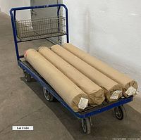 Four large unopened rolls of vinyl wallpaper wrapped in brown paper on a blue metal cart.