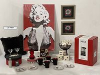 Wide shot showing entire lot: espresso machine box, Marilyn Monroe poster centered, two framed prints above large dice array, black pillow, drinkware including mugs and plates and martini glasses with shaker