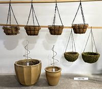 Overall view of two gold ceramic pots with spiral trellises inside, and six hanging baskets including moss and cocoa lined ones hanging from a horizontal bar.