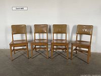 Front view of four vintage wooden library chairs with brown vinyl upholstery on back and seats, lined up against a white wall.