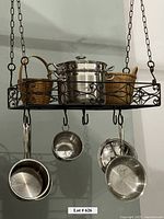 Front and side views of the black metal hanging pot rack with pots, pans, and baskets arranged and hanging from hooks.