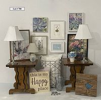 Full lot view showing wooden side tables, lamps, framed artwork, pillows, decorative storage box, vase with faux flowers, and wire basket.
