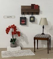 Full view of lot showing hardwood coat rack mounted on wall, small rug on floor, stool with lamp on top, and large faux orchid plant in planter.