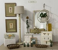 Photo of the lot showing barley twist floor lamp, linen shade, bee canvas artwork, dandelion storage box, circle hanging planter with faux plant, two tobacco baskets, framed fruit artworks, small framed artworks, bolster pillow, and some glassware.