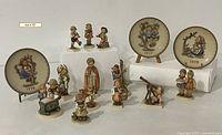 Wide angle image showing entire collection of 15 Hummel figurines and Goebel/Hummel plates with white background
