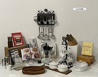 Overview of most kitchen items arranged on a white surface against a blank wall, showing trays, utensils, mugs, cookbooks, and various kitchen tools.