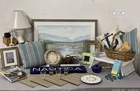 Photo showing large matted and framed watercolor artwork, white lamp, striped pillows, Nautica towel, placemats, and various decorative home items.