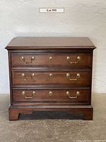Front view of cherry wood chest showing three drawers with brass handles and lock escutcheons.