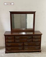 Front view of large cherry finish dresser with mounted mirror showing dental molding and ten drawers with metal handles.