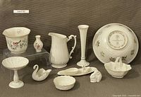 Photo shows collection of Lenox porcelain items including planter, vases, pitcher, bowls, compote, basket, trinket box, and dishes, all in cream color with some decorated and trimmed with gold.