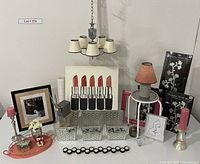 Full lot view showing lipstick artwork, chandelier, framed art, candles, metal tray, baskets, lamp, and other home decor items arranged on white shelf and floor.