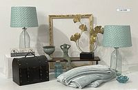 Photo showing full lot setup on white table with both teal glass lamps, treasure chest, blanket, shelf brackets with wooden shelf, gold ginkgo leaf sculpture, teal glass bottle, lotus candle holder, pedestal planter, coasters and picture frame.