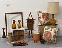 Photo shows overall lot contents including decorative items arranged on a surface with a beige lamp, two floral pillows, glass bottles, trays, and other decorative accessories