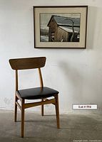 Photo of the wooden chair with black seat along with the framed watercolor artwork hanging on the wall above it