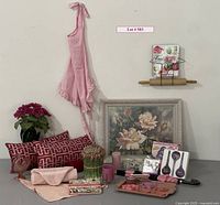 Wide arrangement of lot items showing artwork, pillows, pink kitchen and decorative items, and aprons.