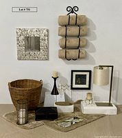 Image showing heavy duty iron towel rack with four tan towels mounted on wall, two nonslip rugs, large woven basket, a black wooden box, a jewelry stand with pearl necklace, mirrored gold tray, candles with holders, small countertop lamp, and framed artwork.