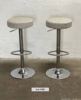 Pair of modern adjustable chrome bar stools with fabric cushions shown frontally