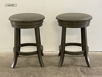 Front view of two round gray-green counter stools with nailhead trim showing their design and condition.