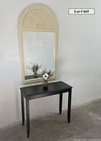 Wide view of painted wood Palladian mirror above black wooden hall table with faux floral arrangement on the table