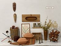 Wide shot of entire lot showing masks, large basket with smaller baskets inside, framed artwork, wooden bowls, painted juggle sticks, candlesticks, glass vases, ceramic pot with faux branches, metal wall baskets, striped textile, and clay cookers.