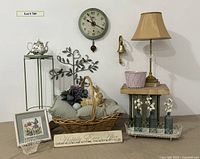 Overview of the clock, table, wicker basket with pillows and resin rabbit, floral teapot on metal stand, and decor items arranged for lot display