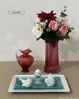 Photo showing raspberry colored Fenton glass pitcher and vase with faux flowers, white ceramic tray with miniature hand-painted Fenton glass figures (bird, rabbit, Easter egg), and teal art glass tray.