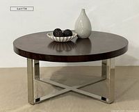Front view of the round coffee table showing thick dark wooden top and shiny chrome base with decorative bowl and vase on top.